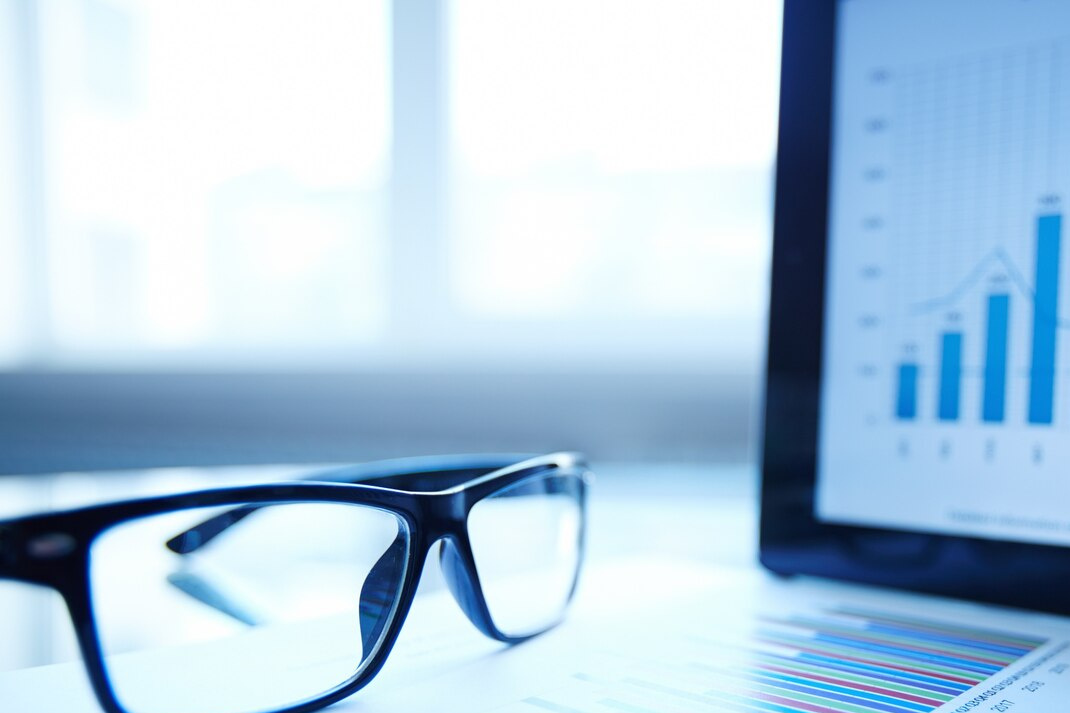 Eyeglasses in focus with blurred graph on computer screen in background.